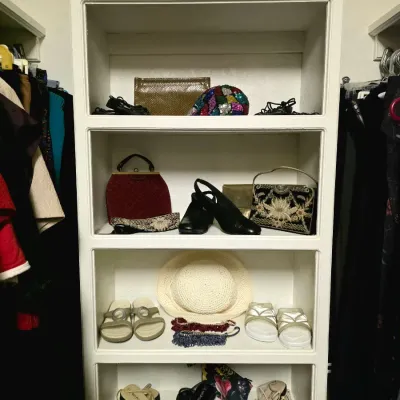 White shelving unit displaying an assortment of women's vintage accessories, including evening bags, heels, sandals, bead necklaces,...