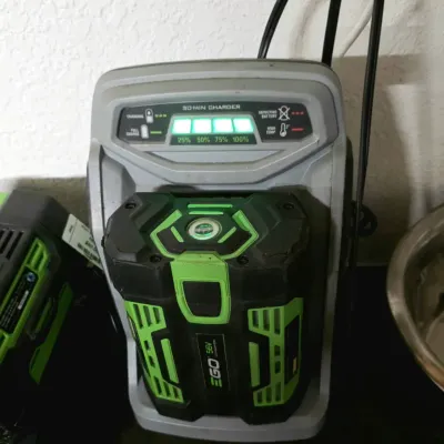 EGO Power+ 56V lithium battery connected to a 30-minute fast charger showing a full charge indication.