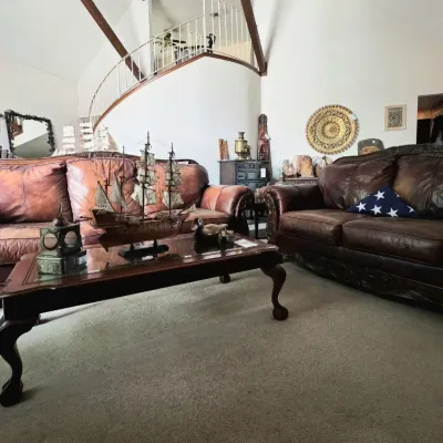 Traditional living room set featuring dark leather sofa and loveseat with carved wood trim, accompanied by a glass-top coffee table...