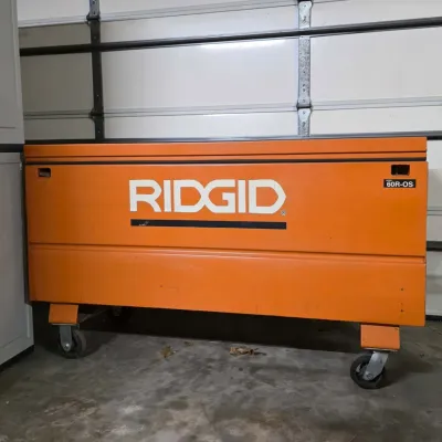 Large orange Ridgid model 60R-OS heavy-duty steel jobsite storage chest mounted on swivel casters.