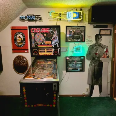 Williams Cyclone pinball machine from 1988, surrounded by various bar memorabilia including neon signs, framed prints, and a Humphrey...