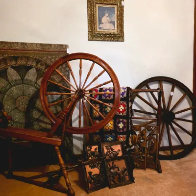 Vintage wooden spinning wheel and a large wooden wagon wheel, displayed alongside framed artwork, a colorful crochet blanket, and rustic...