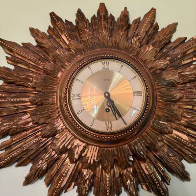 Vintage Welby sunburst wall clock featuring a gilded, ornate starburst frame and a gold-tone dial with Roman numerals.