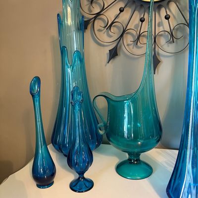 Sale Photo Thumbnail #194: Collection of mid-century modern blue and teal swung glass vases and a pitcher, displayed in front of a vintage starburst wall clock.