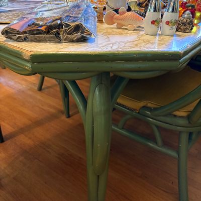 Vintage green-painted bamboo-style dining table with a faux-marble laminate top, surrounded by matching chairs with yellow cushions.