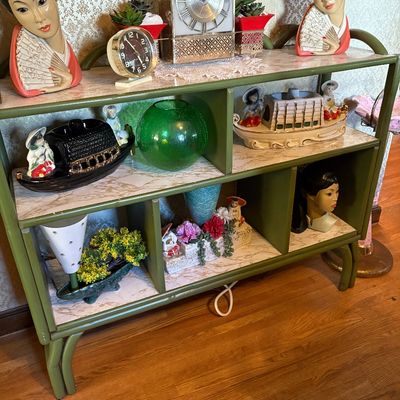 Mid-century modern green bamboo-style shelving unit displaying a collection of vintage Asian-inspired decor, including ceramic geisha...