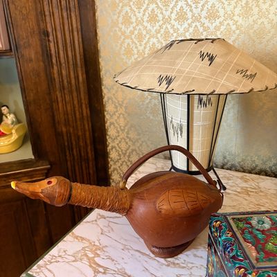 Vintage leather-wrapped duck-shaped decanter or canteen alongside a mid-century modern table lamp with a fiberglass shade.