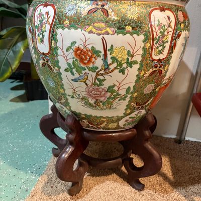 Sale Photo Thumbnail #232: Large Chinese Famille Rose style porcelain fish bowl planter, featuring hand-painted floral and bird motifs with gold accents, resting on a carved dark wood stand.