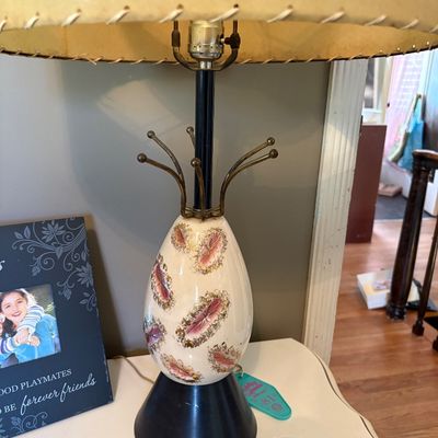 Sale Photo Thumbnail #173: Mid-century modern table lamp featuring an egg-shaped ceramic body with pink and gold accents, a black cone base, and a whipstitched fiberglass shade.