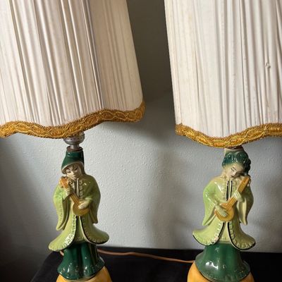 Sale Photo Thumbnail #285: Pair of mid-century ceramic table lamps featuring Asian-style figures playing stringed instruments, complete with pleated fabric shades trimmed in gold fringe.