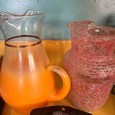 Sale Photo Thumbnail #213: Mid-century glass pitchers, featuring a frosted orange ombre pitcher with a gold band and a clear pitcher with a pink and white spaghetti-spun glass texture.