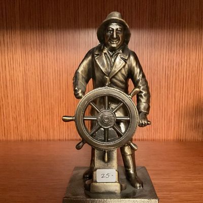Vintage cast metal figurine of a sea captain at the ship's wheel, featuring a bronze-tone finish and mounted on a square base.