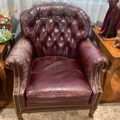 Vintage oxblood leather tufted armchair with brass nailhead trim, showing significant wear and cracking on the armrests. Matching ottoman. 