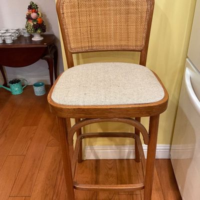 Bentwood barstool with a woven cane backrest and a light-colored upholstered seat cushion.