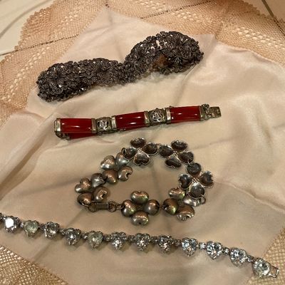 Collection of vintage bracelets, including an ornate silver floral cuff, a red carnelian or glass panel bracelet with silver-tone...