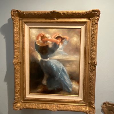 Impressionistic oil painting depicting a woman in a blue dress adjusting her hat before a mirror, housed in an ornate, gilded gesso frame.