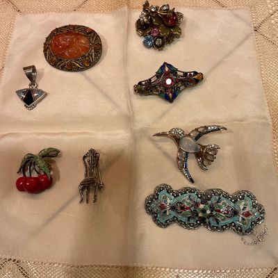 Collection of vintage costume jewelry brooches and pendants, including a carved carnelian-style brooch, a hummingbird pin, and a cherry...