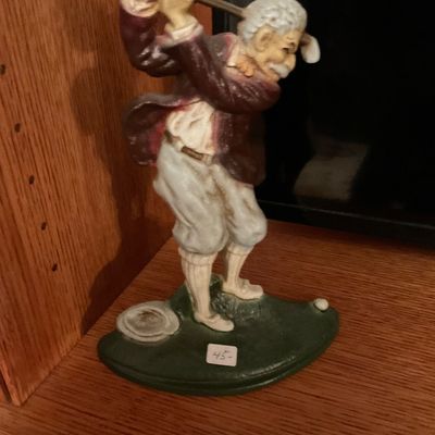 Vintage painted cast iron doorstop depicting an elderly golfer mid-swing, mounted on a green base.