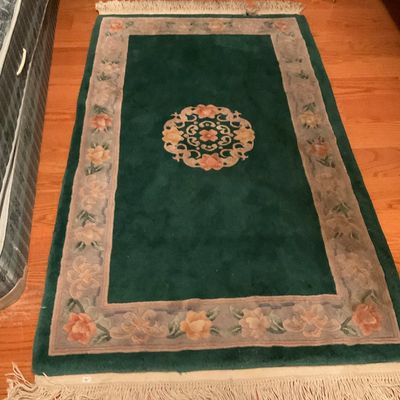 Chinese Art Deco style wool rug featuring a deep green field with a central floral medallion, a beige floral border, and fringed ends.