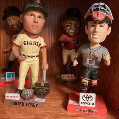 Collection of San Francisco Giants bobbleheads, including Buster Posey, Hunter Pence, and Cody Ross, displayed on a wooden shelf.