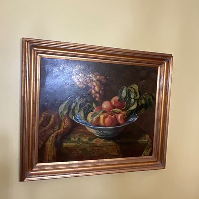 Still life oil painting depicting peaches and grapes in a bowl, housed in a classic gilded wooden frame.