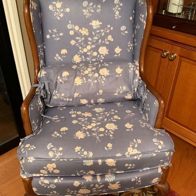 Vintage wingback armchair upholstered in a blue and cream floral fabric, featuring a matching bolster pillow and carved wooden legs.