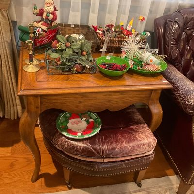 Traditional wooden end table with cabriole legs, displaying various Christmas decorations, paired with a matching tufted leather ottoman...