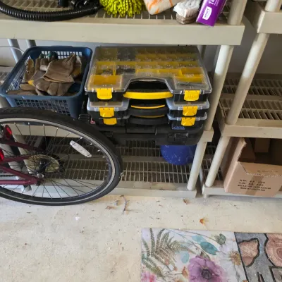 Sale Photo Thumbnail #102: Stack of yellow and black plastic organizer cases alongside a basket of work gloves on a plastic shelving unit, with a bicycle wheel visible in the foreground.