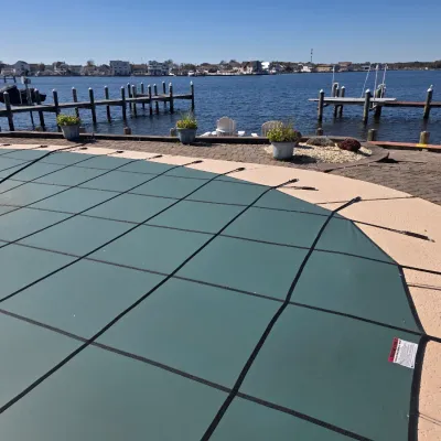 Sale Photo Thumbnail #43: Green mesh safety pool cover secured with straps on a concrete deck, overlooking a waterfront dock area.
