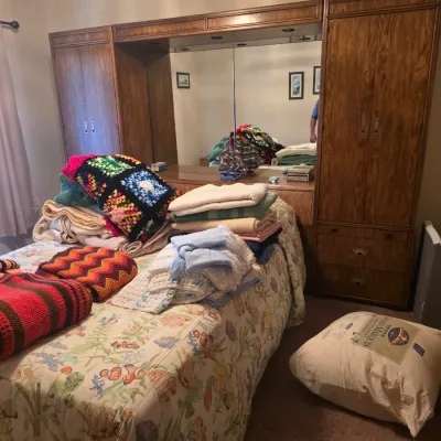 Sale Photo Thumbnail #78: Vintage mid-century modern style wooden bedroom wall unit with integrated headboard, mirrors, and wardrobes, shown with an assortment of colorful crocheted blankets and quilts.