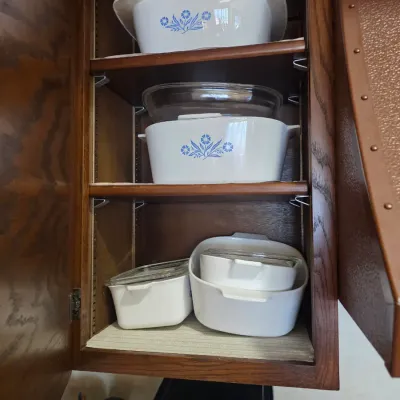 Sale Photo Thumbnail #61: Vintage Corning Ware Blue Cornflower casserole dishes and baking pans stored in a wooden kitchen cabinet.