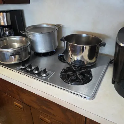 Sale Photo Thumbnail #56: Vintage stainless steel drop-in gas cooktop with four burners and front-mounted control knobs, shown with various stainless steel stockpots.