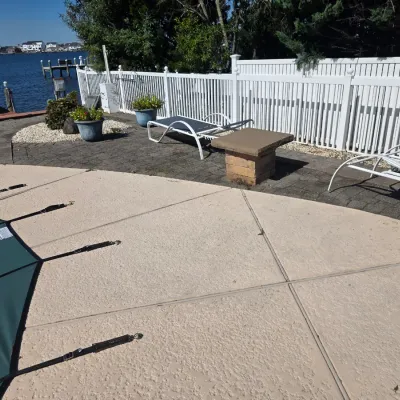 Sale Photo Thumbnail #42: Pair of white metal frame chaise lounge chairs with dark mesh fabric, shown alongside a small stone side table on a paved patio area.