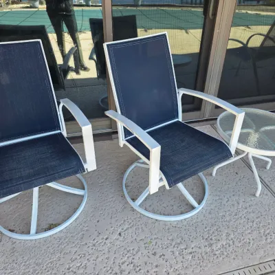 Sale Photo Thumbnail #35: Pair of white metal swivel patio chairs with dark blue mesh fabric, accompanied by a matching small round glass-top side table.
