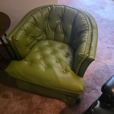 Sale Photo Thumbnail #117: Mid-century modern tufted barrel chair upholstered in avocado green vinyl, featuring a curved back and button detailing.