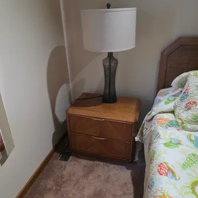 Sale Photo Thumbnail #11: Mid-century modern style two-drawer wooden nightstand with a sunburst veneer pattern on the drawer fronts, topped with a tall glass table lamp.