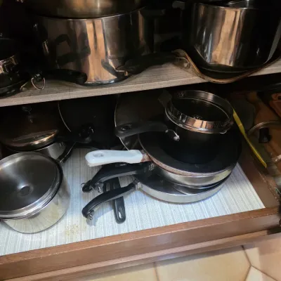 Sale Photo Thumbnail #70: Assorted stainless steel and non-stick pots, pans, and lids stored in a kitchen cabinet drawer.
