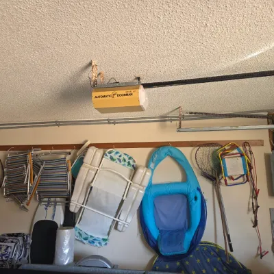 Sale Photo Thumbnail #110: Assorted garage items including folding lawn chairs, a blue pool float, a fishing net, and a vintage Automatic Doorman garage door opener mounted on the ceiling.