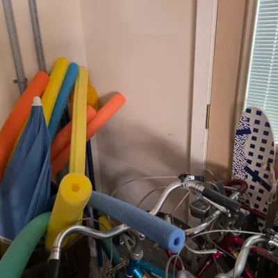 Sale Photo Thumbnail #96: Assorted pool noodles, a blue umbrella, and vintage Schwinn Varsity bicycles stored in a corner.