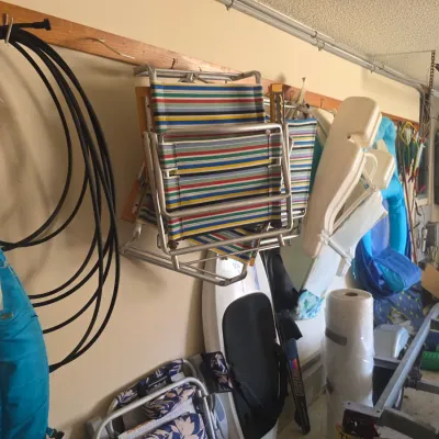 Sale Photo Thumbnail #98: Assorted garage and outdoor gear, including vintage striped folding lawn chairs, a surfboard, and pool floats hanging on wall mounts.