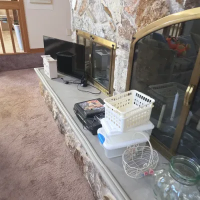 Sale Photo Thumbnail #34: Assorted household items including a flat-screen television, a VCR, plastic storage baskets, and decorative glassware arranged on a stone fireplace hearth.