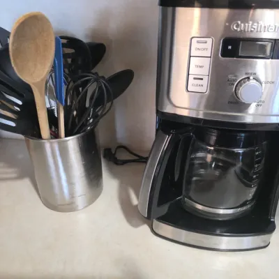 Sale Photo Thumbnail #60: Cuisinart programmable 14-cup coffeemaker in stainless steel and black, shown next to a stainless steel utensil holder filled with kitchen tools.