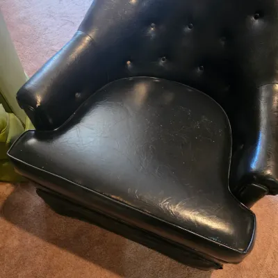 Sale Photo Thumbnail #120: Vintage mid-century tufted black vinyl club chair, showing some wear on the seat edge and missing one button on the backrest.