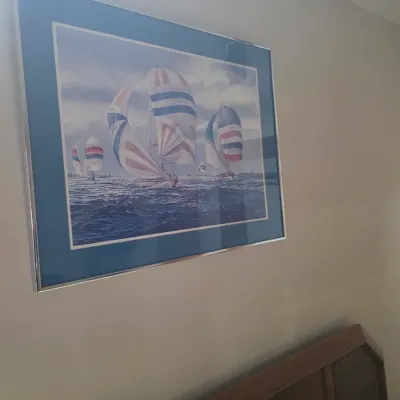 Sale Photo Thumbnail #13: Framed maritime art print depicting sailboats with colorful spinnakers on choppy water, housed in a silver-tone metal frame with a blue mat.