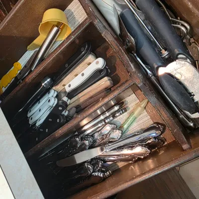 Sale Photo Thumbnail #67: Assorted kitchen utensils and flatware, including steak knives, butter knives, and a can opener, organized in a wooden drawer divider.