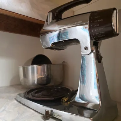 Sale Photo Thumbnail #84: Vintage Sunbeam Mixmaster stand mixer with a chrome finish and brown accents, accompanied by a stainless steel mixing bowl.