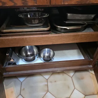 Sale Photo Thumbnail #65: Assorted kitchenware including baking sheets, a glass bowl, metal roasting pans, and stainless steel mixing bowls stored on pull-out wooden cabinet shelves.