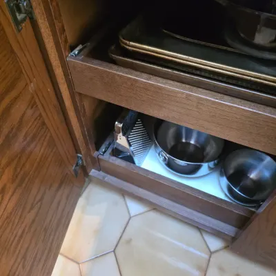 Sale Photo Thumbnail #69: Assorted kitchenware including baking sheets, stainless steel mixing bowls, and a box grater, stored in pull-out wooden cabinet drawers.