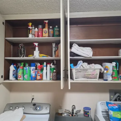 Sale Photo Thumbnail #72: Assorted household cleaning supplies, laundry detergents, and linens organized inside white laundry room cabinets.