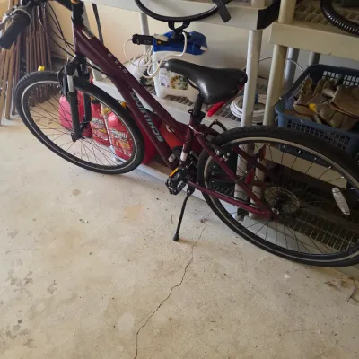 Sale Photo Thumbnail #101: Schwinn GTX 1 hybrid bicycle in a maroon finish, featuring front suspension, multi-speed gearing, and a kickstand.